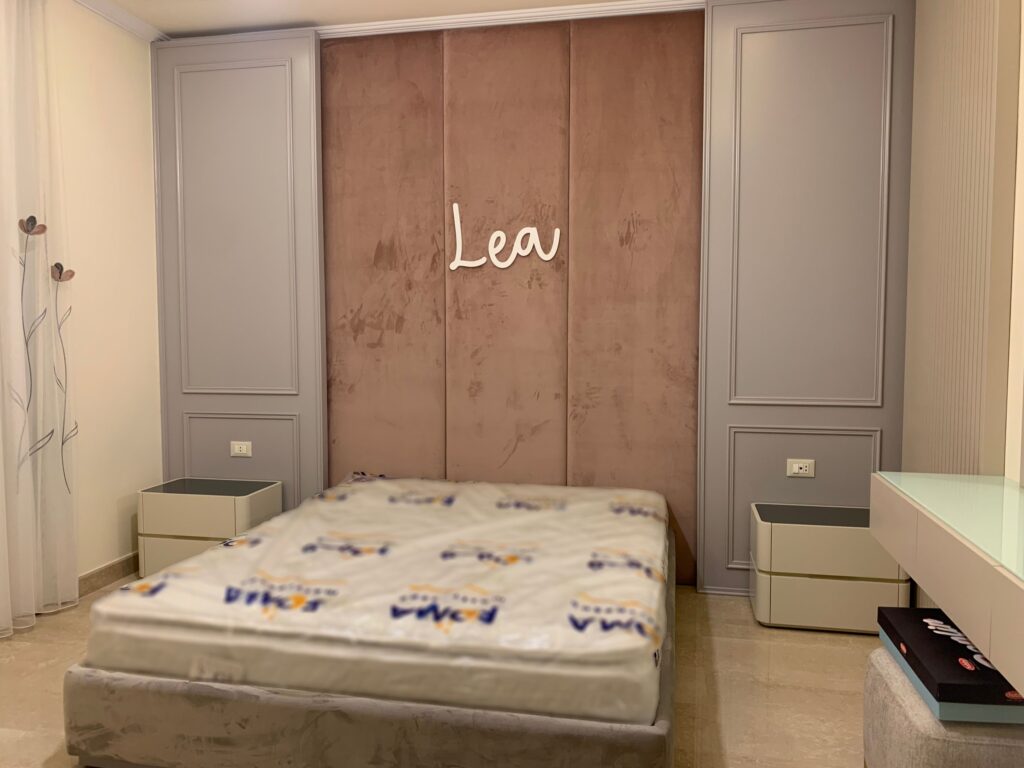 Bed with pink quilted headboard containing the girl's name