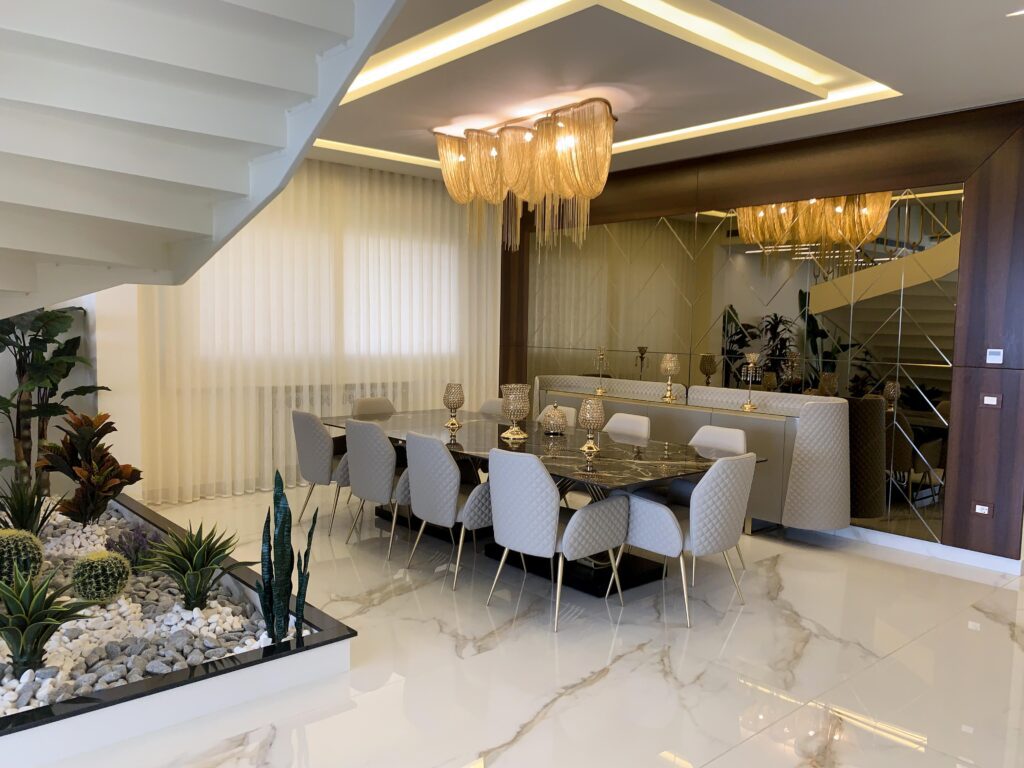 A luxurious design of a dining area next to the stairs. With a custom made mirror-wall, a ceramic top dining table, and 10 quilted chairs along with a sideboard