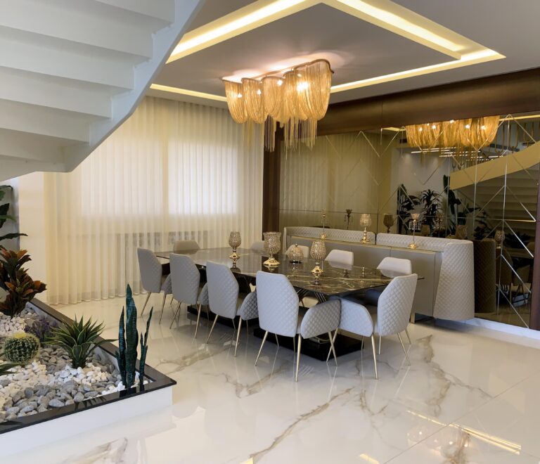 A luxurious design of a dining area next to the stairs. With a custom made mirror-wall, a ceramic top dining table, and 10 quilted chairs along with a sideboard